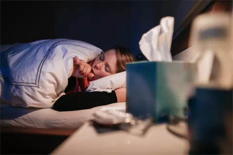 Frau liegt im Bett und hustet